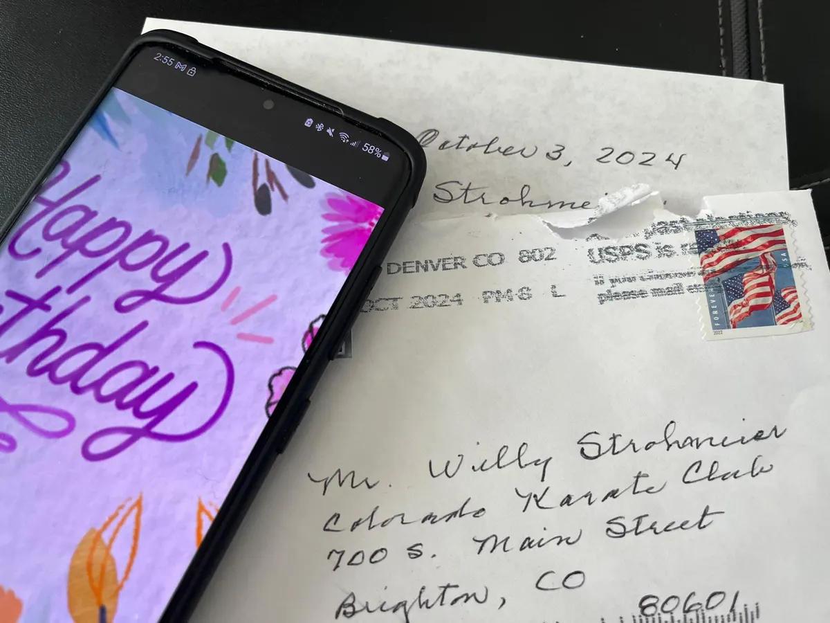 Phone showing a Happy Birthday e-card on top of a handwritten letter addressed to Colorado Karate Club