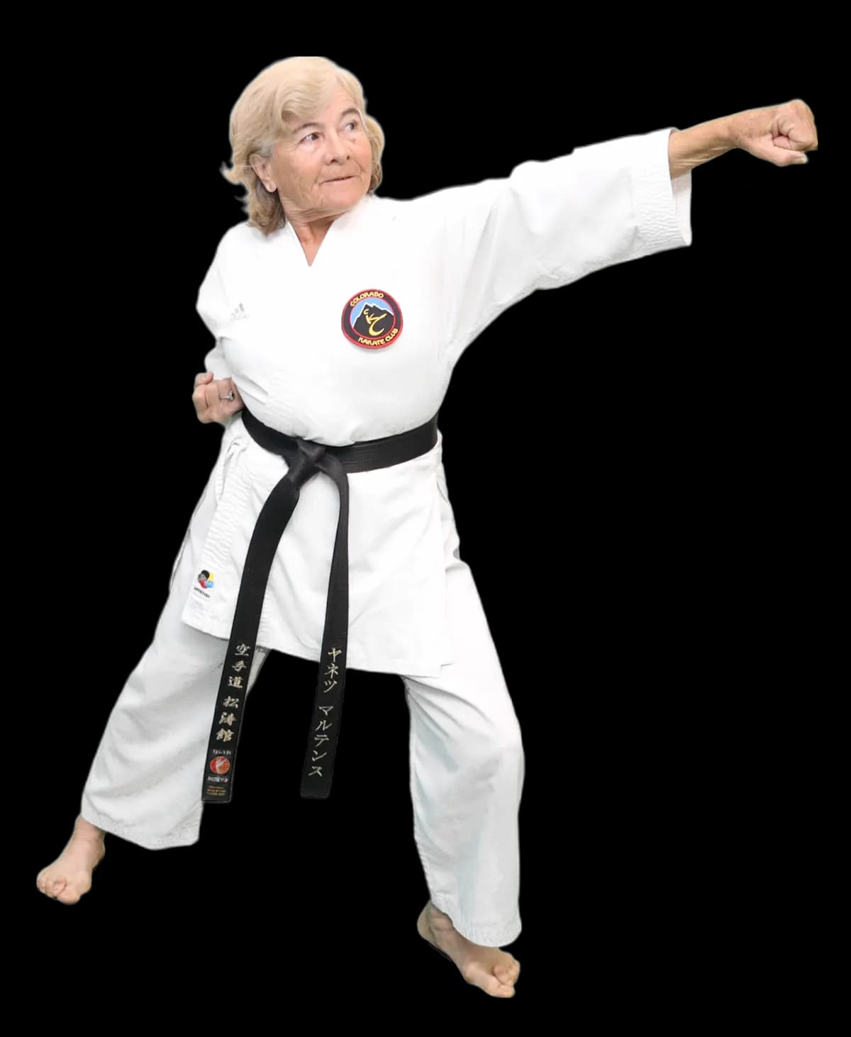 Older woman in a Colorado Karate Club gi and black belt throwing a punch in a karate stance