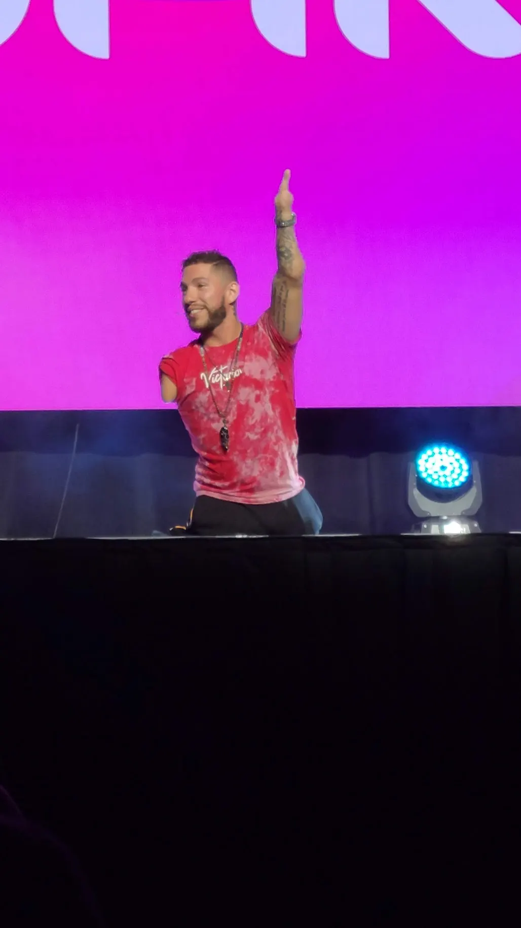 Smiling speaker with one arm raised high on a stage in front of a bright pink screen